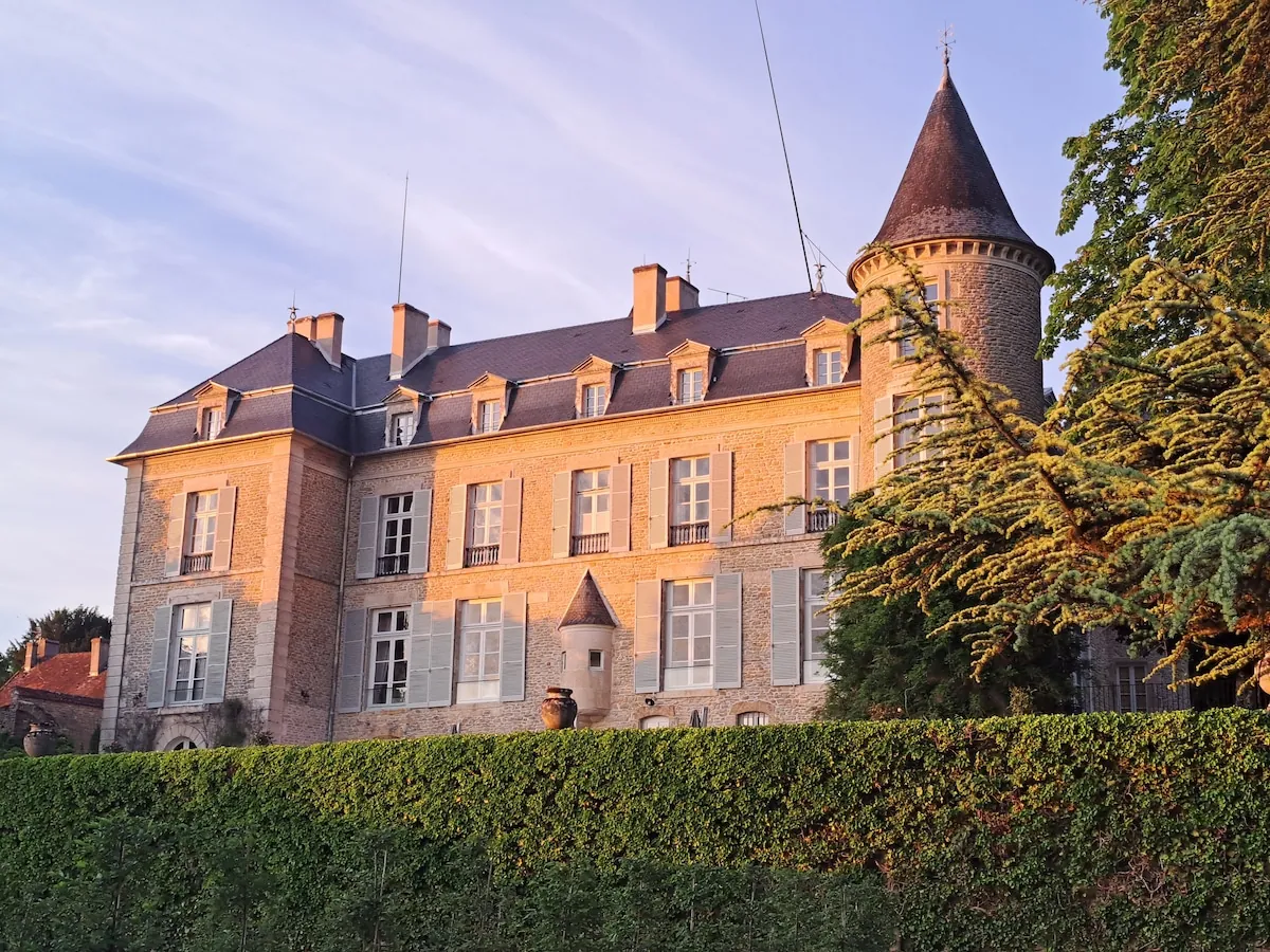 Fasada Château de Tharoiseau z okrągłą wieżą w popołudniowym słońcu